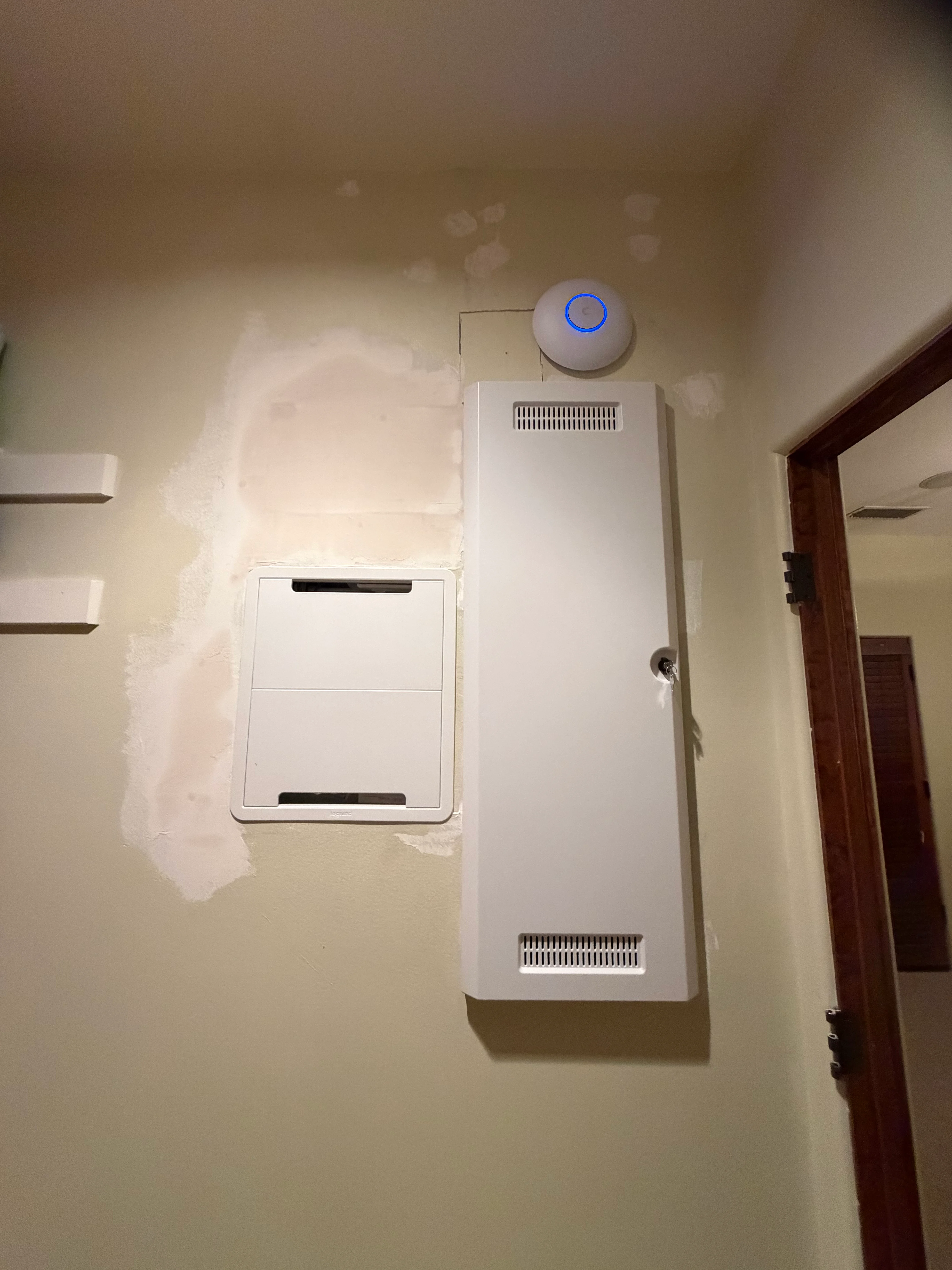 White in-wall data rack with ventilation ports and wireless control button installed in drywall