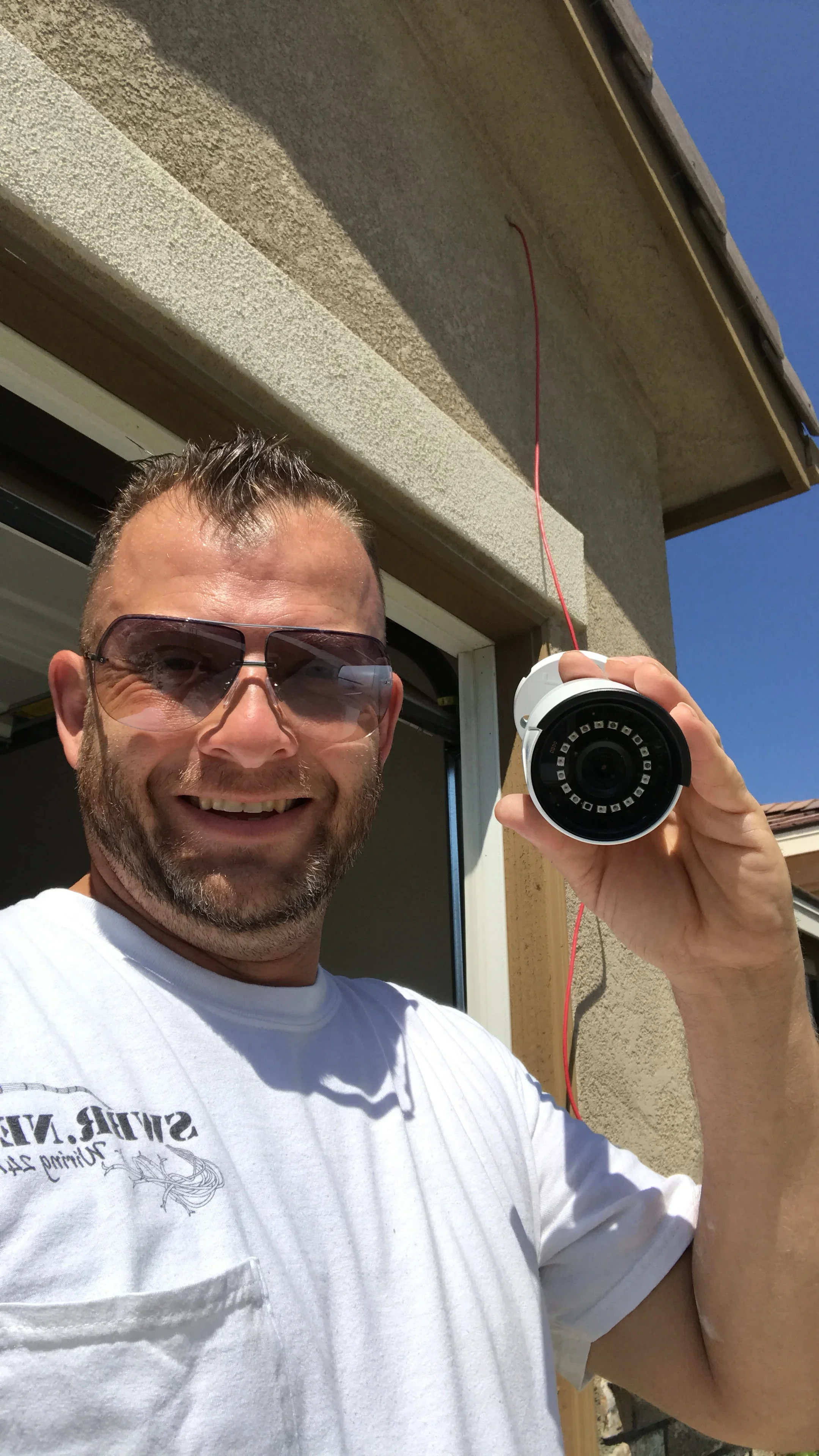 Technician holding installed white security camera with IR LEDs on residential building exterior