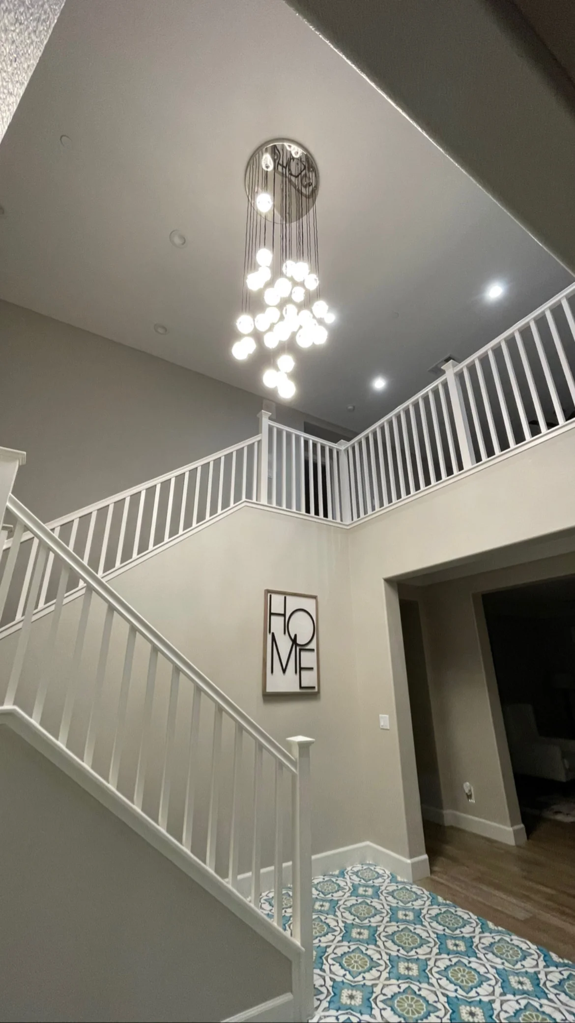 Modern chandelier with white globe pendants installed in two-story foyer with white railings