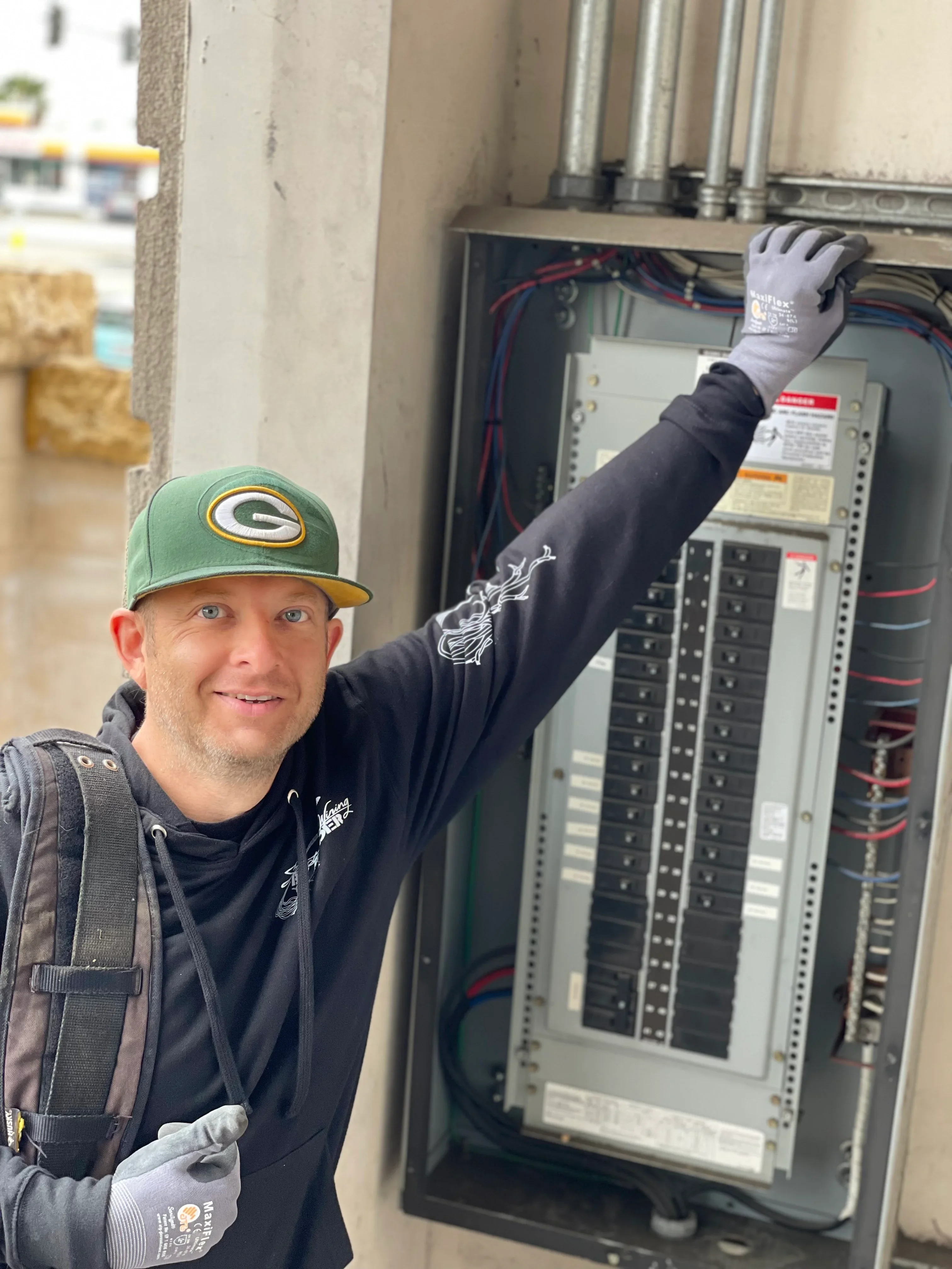 Electrician in safety gloves working on installed electrical panel with organized breakers and wiring