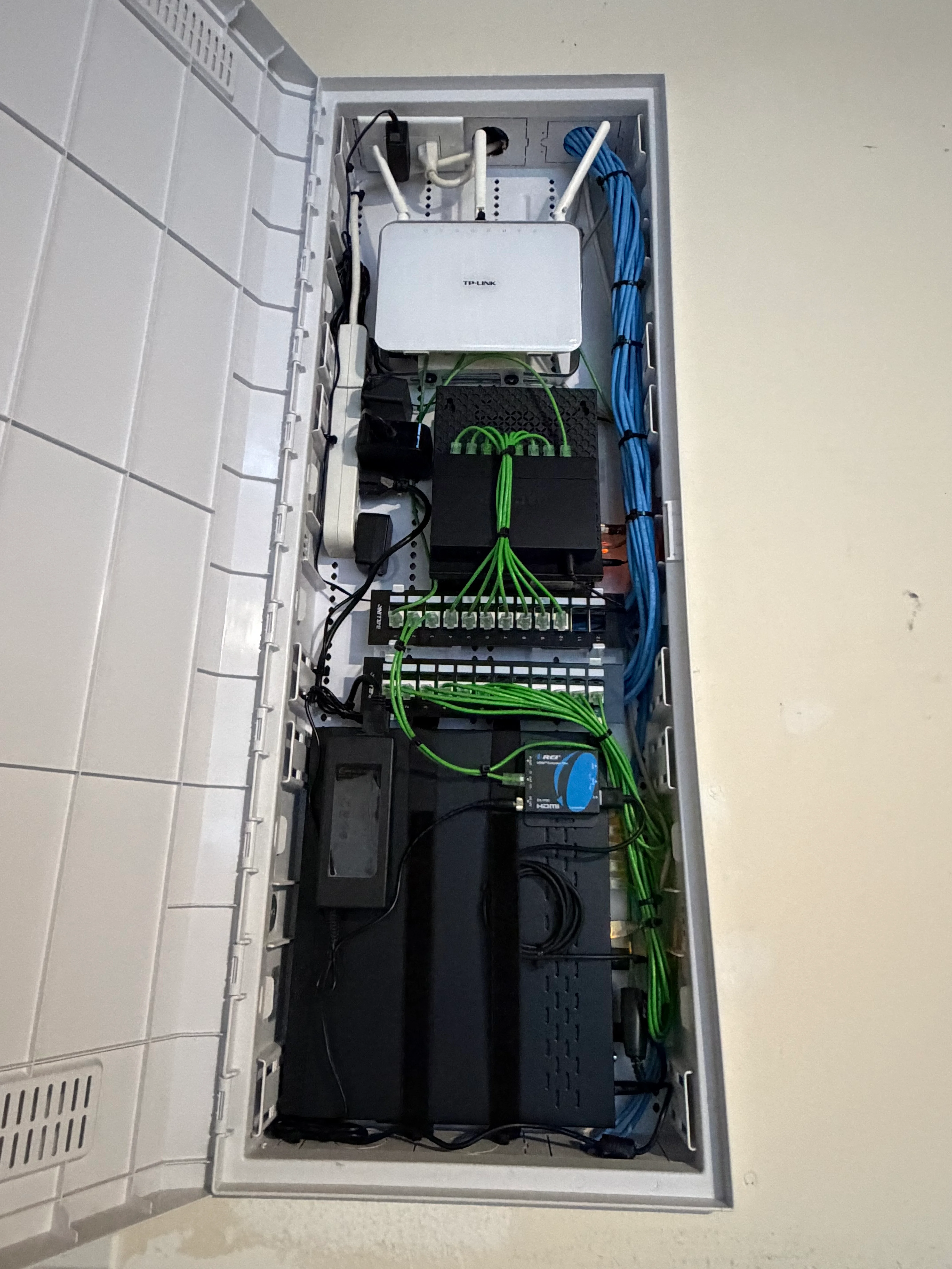 Wall-mounted network panel with router, patch panels, and organized green and blue ethernet cabling