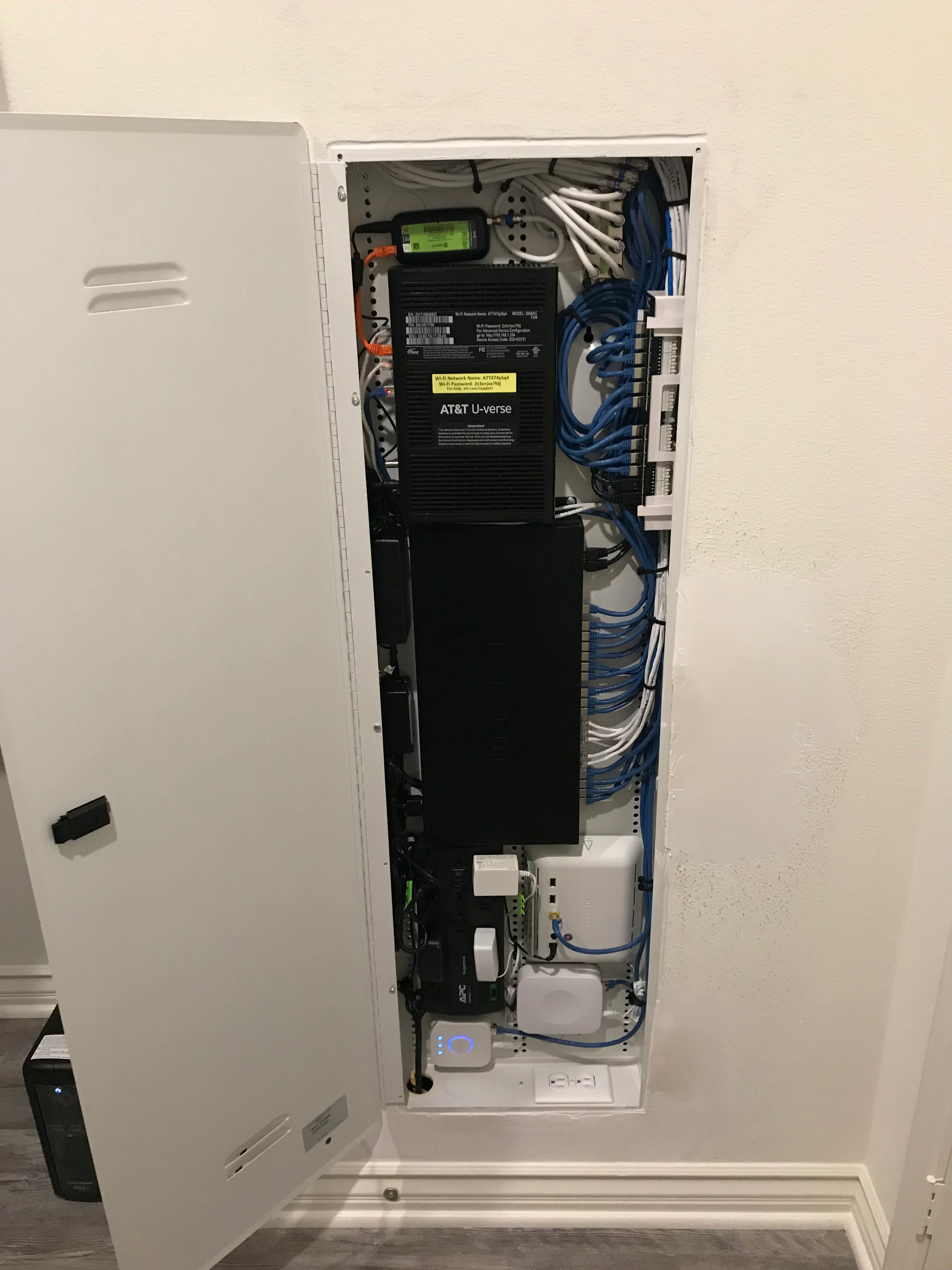 Interior view of white wall-mounted structured wiring panel with AT&T U-verse equipment and organized blue network cabling