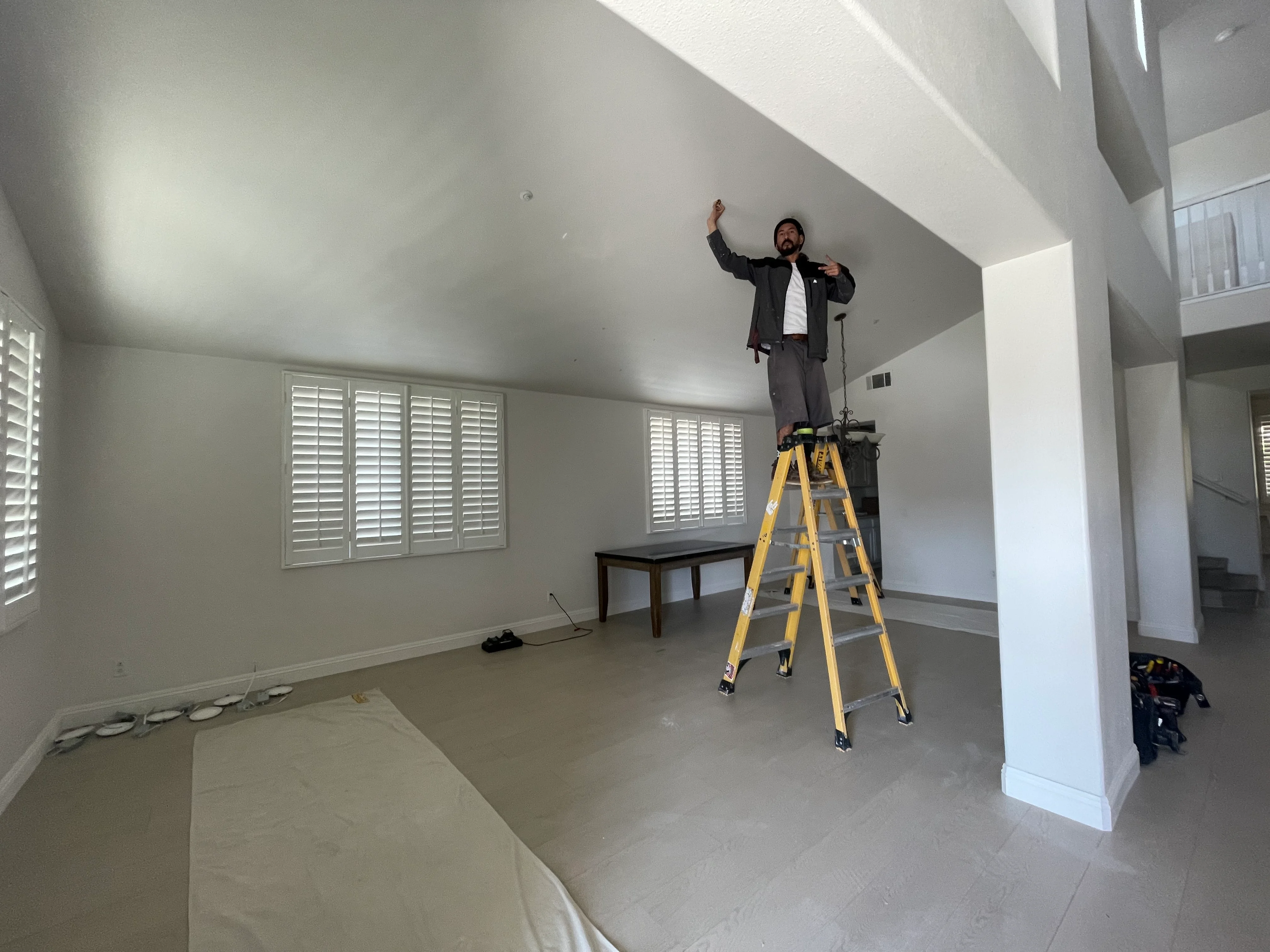 Electrician on ladder measuring ceiling for light fixture installation in modern home